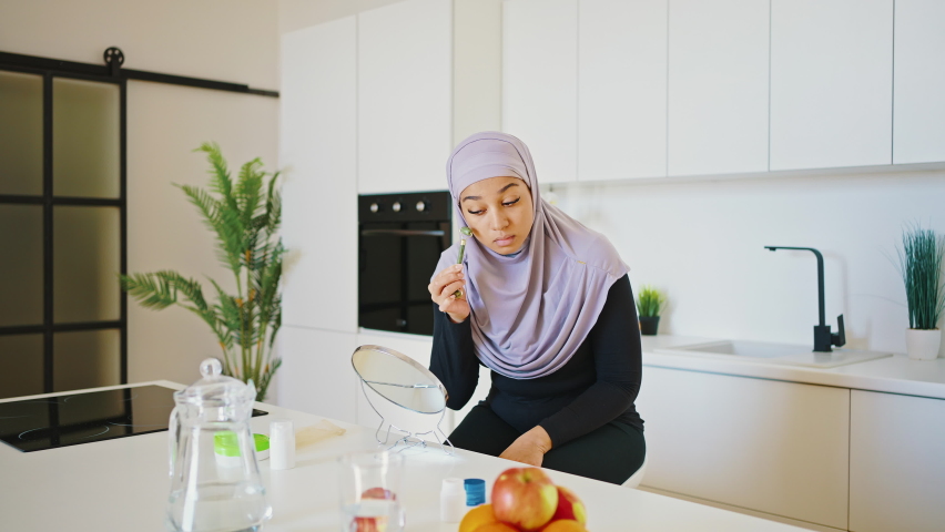 Young woman in a Muslim hijab gives herself a facial massage using a jade roller. Facial care with natural stones