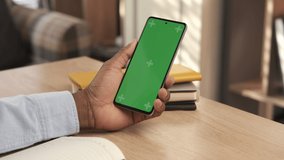 African american man using mobile phone vertical green screen. Male holding portable gadget close up indoors home living room. Mock-up for tracking. Watching content video blog and surfing internet