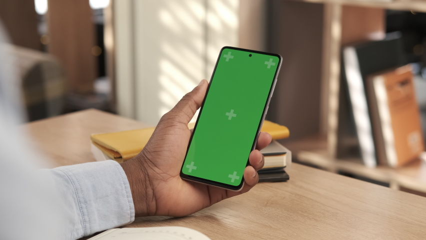 African american man using mobile phone vertical green screen. Male holding portable gadget close up indoors home living room. Mock-up for tracking. Watching content video blog and surfing internet Royalty-Free Stock Footage #1069434436