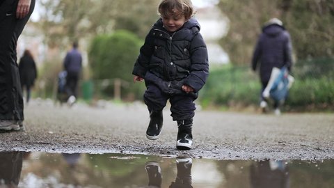 Cute toddler jumping into puddle of water. Adorable child boy playing with puddle in slow-motion