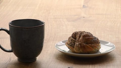 Time for a coffee break as black coffee is being poured into a mug. On the wooden table is also a plate with a cardamom bun. Footage made in Sweden.