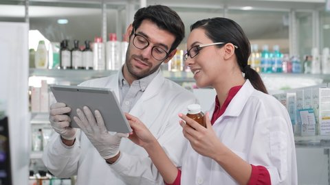 Male and female pharmacist using a digital tablet checking stock inventory in modern pharmacy. Slow Motion - Βίντεο στοκ