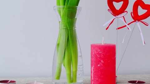 Holiday. Tulip flowers in glass vase on wooden table background wall at home, close up. Burning red candle Mothers Womans Valentines Day design concept.