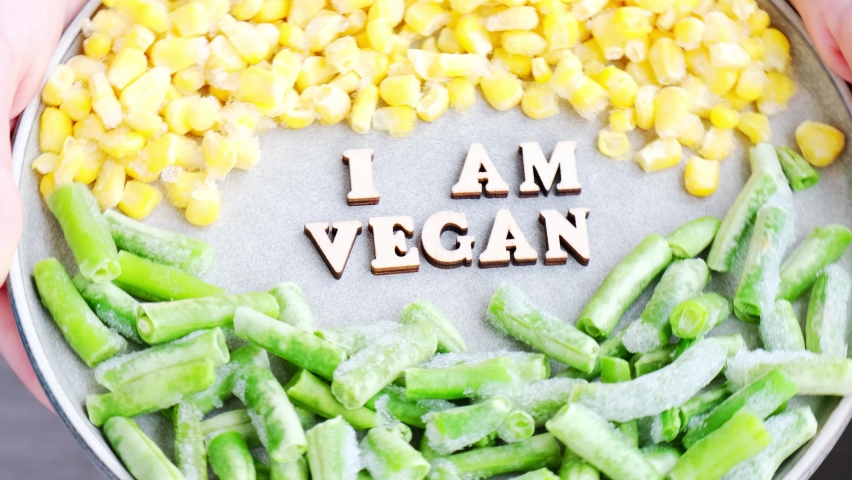 Female hands hold I AM VEGAN text in plate. Veganism, vegetarian healthy lifestyle green beans yellow corn. Healthy eating vegan. Wooden letters