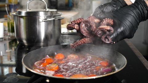 Chef putting octopus tentacles into frying pan with boiling broth. Juicy octopus tentacles in restaurant kitchen. Cooking process of octopus french style, Restaurant gourmet dish. 4 k video