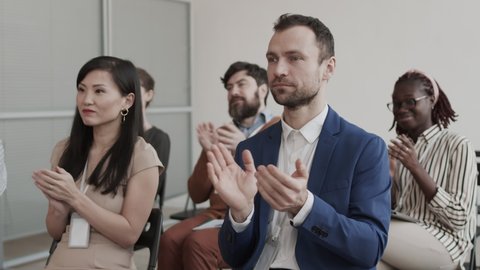 Medium long shot of multiethnic business women and men sitting in conference room, smiling and clapping hands Video Stok
