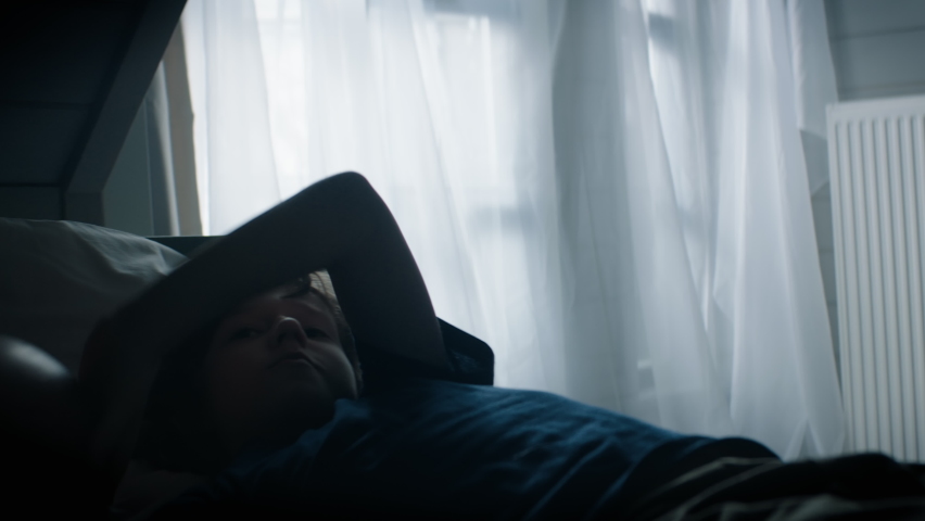 CU Silhouette portrait of cute little Caucasian kid boy playing with football ball in his attic bedroom at home. Shot with 2x anamorphic lens