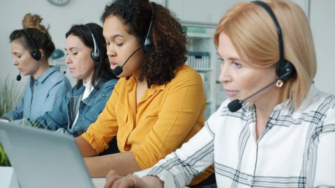 Diverse group of women are making calls using headsets and laptops working in call center busy with communication and customer support. Business and telephony concept. 스톡 비디오