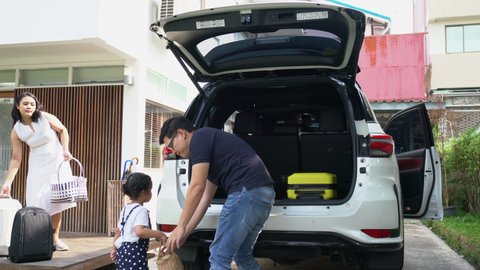 Happy Asian family on road trip vacation. Father and mother with cute baby daughter loading luggage inside car trunk. Parents with child girl kid enjoy and having fun outdoor weekend activity together