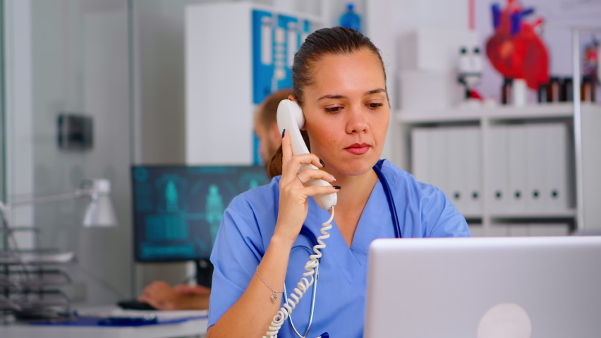 Medical practitioner answering phone calls and scheduling appointments in hospital. Healthcare physician in medicine uniform, receptionist doctor assistant helping with telehealth communication | Shutterstock HD Video #1069455700