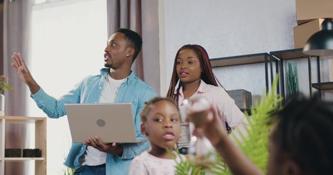 Adorable satisfied modern young african american couple with kids standing in their newly acquired apartment and planning how to furnish dweling to their preferences: stockvideo