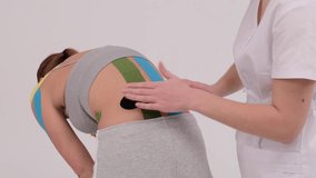 Demonstration video of a therapist taping kinesio tape on a female patients back. Pain treatment. Sport and rehabilitation