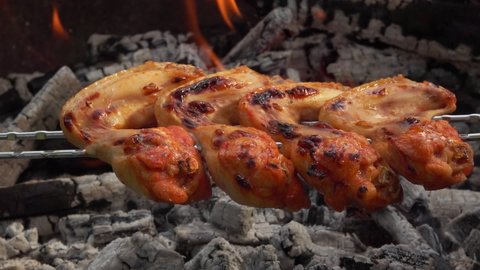 Fresh chicken wings on the skewers are roasting above the coals outdoors in rapid footage