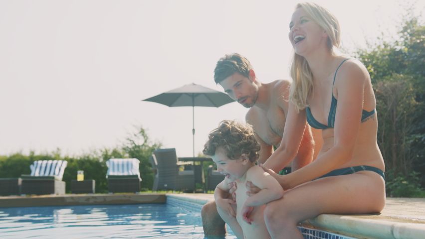 Family with young son sitting on edge of outdoor pool playing and having fun on summer vacation - shot in slow motion | Shutterstock HD Video #1069462144