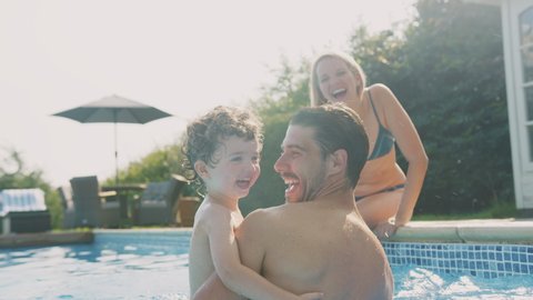 Father with young son playing and having fun on summer vacation in outdoor swimming pool as mother sits on edge - shot in slow motion