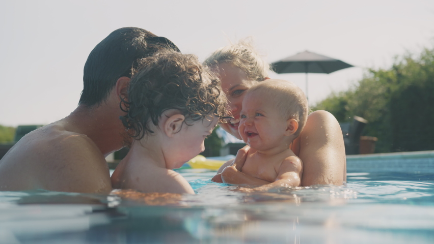 Family with young son and baby daughter playing and having fun on summer vacation in outdoor swimming pool - shot in slow motion