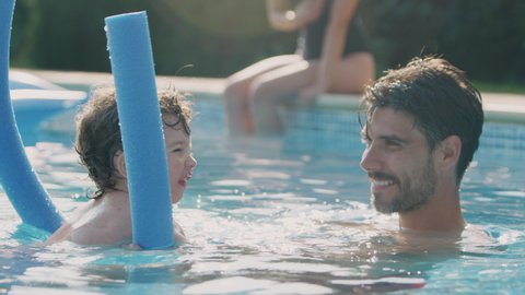 Father teaching son to swim on summer vacation in outdoor swimming pool using floatation aid - shot in slow motion