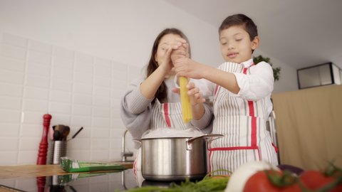In the kitchen: A single-parent family cooking pasta together. Mother and son putting pasta to boil. Children helping parents.  