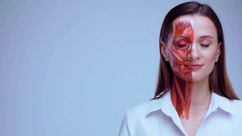 Young woman with half of face with muscles structure under skin pointing to looking left on copy space.. Model for medical training on a light background. Close up video of face human anantomy.