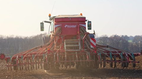 Perry Green, Much Hadham, Hertfordshire. UK. March 22nd 2021. Rear view of a tractor sowing seeds with a seeder driller in a field in the late afternoon.