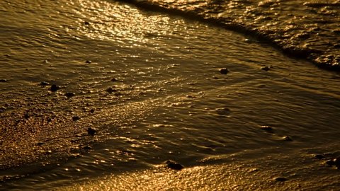 Sun glare on the golden wave in the surf zone on a sandy beach. Natural background with sun glints on surface of water. Texture of water surface of sea reflection of sun's rays. Close-up (4K-60pfs)