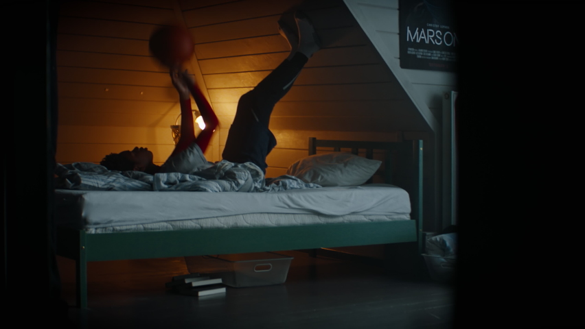 WIDE Bored African American Black kid teenager boy playing with basketball in his attic bedroom at home. Shot with 2x anamorphic lens Royalty-Free Stock Footage #1069471750