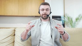 young bearded man in casual clothes with headset meeting online, conference or business course, webinar or video call. Man talking to the camera working at home Webcam view. Explain and speak remotely