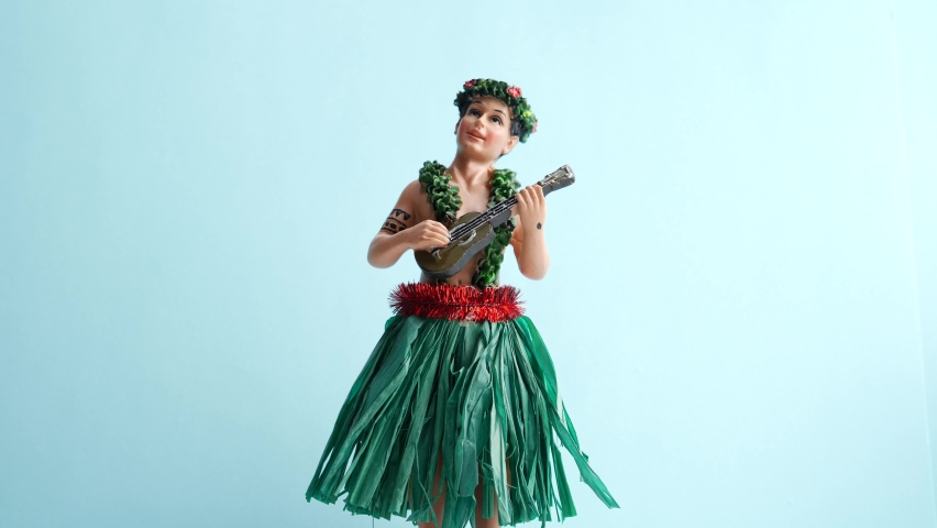 Isolated dancing hula boy doll against blue background shaking against light blue background