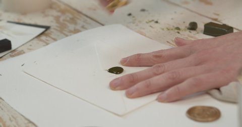 An artisan pressing a stamp over hot wax on the edge of an envelope, in order to seal it (old-style). Handheld shot.
