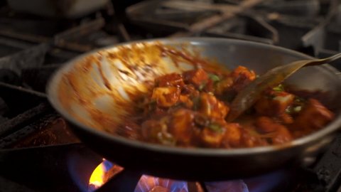 Paneer tikka masala tossed in pan over fire in restaurant kitchen, close up slow motion 4K