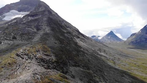 Aerial view between mountain peaks, in the highlands of Jotunheimen National park, sunny, summer day, in Oppland, Norway - pan, drone shot