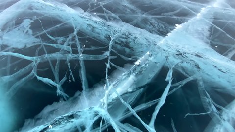 Exciting ice skating on the frozen Lake Baikal. View from above. Close-up. Blue transparent clear smooth ice with deep cracks. Natural landmark of Russia.