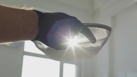 Close-up of male hand sieving flour in sunrays. Camera follows bakery ingredient falling in metal bowl in sunlight. Unrecognizable Caucasian chef baker working in candy store kitchen.