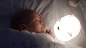 newborn baby boy falling asleep in a crib in evening, 3-week-old little boy looking at night light