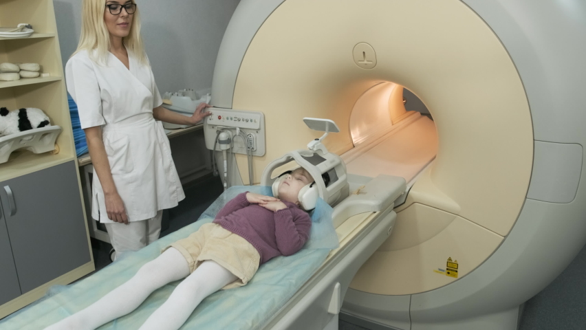 Woman doctor radiologist makes an MRI scanning of brain, head, neck for patient little girl, girl lies on automatic table, using modern equipment, coil on the head, headphones | Shutterstock HD Video #1069482508