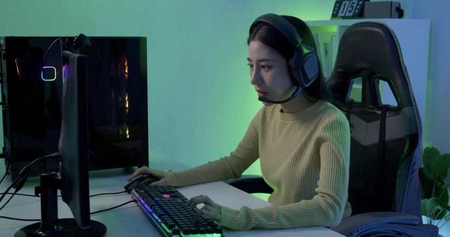 Young Asian woman gamer having live stream and playing in Online Video Game. She playing and winning in video games on a computer. She playing online games with neon lights background. | Shutterstock HD Video #1069483438