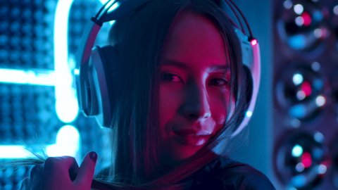 Stylish Woman Listening Music in Headphones and Dancing Energetic and Rhythm in Pink and Blue Light. Pretty and Attractive 30s Asian Girl Looking at Camera Indoors Colourful Purple Neon CloseUp 4K