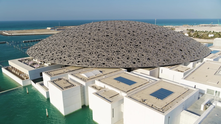 Abu Dhabi, United Arab Emirates - 16 March 2021: Aerial view of Louvre Abu Dhabi, a contemporary architecture building museum along the sea with city skyline in background, United Arab Emirates.
