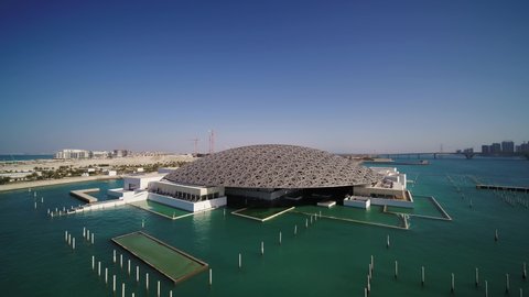 Abu Dhabi, United Arab Emirates - 16 March 2021: Aerial view of Louvre Abu Dhabi, a contemporary architecture building museum along the sea with city skyline in background, United Arab Emirates.