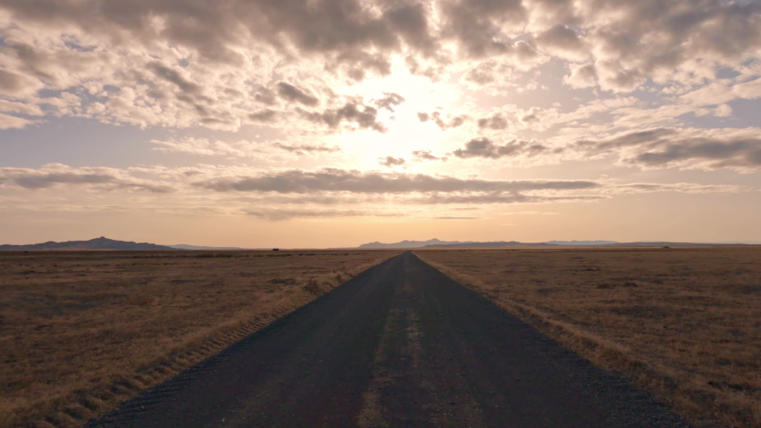 Driving on dirt road over flat vast Utah desert towards the sun glowing behind the clouds.