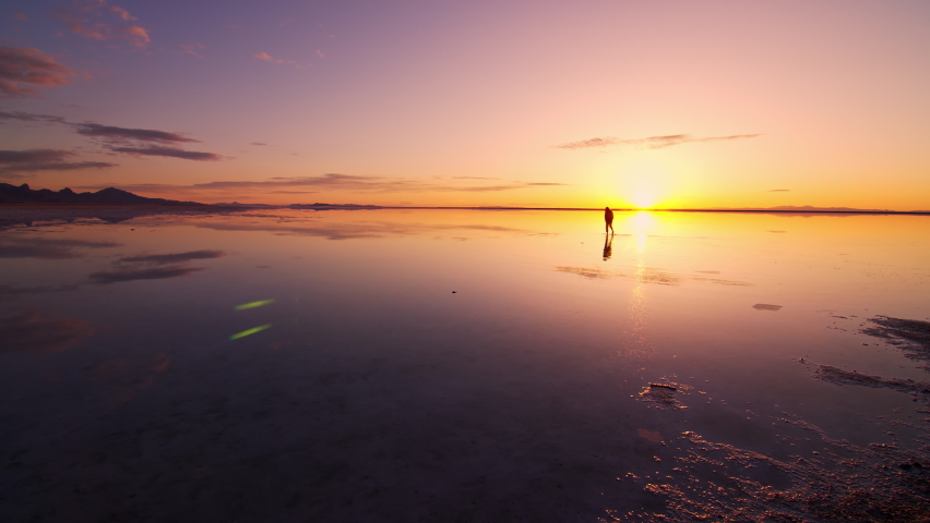 Person standing in water covering the Bonneville Salt Flats during sunrise as colors reflect in the lake.