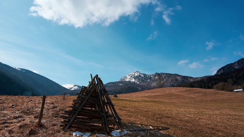 Rural mountain landscape after winter, blue sky with clouds, fence and hay dryers