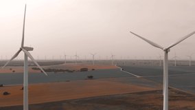 Drone point wide angle aerial view of moving turbines of windmills. Wind energy converter into electricity. Panoramic real time video of cultivated farm lands during gloomy day. Europe, Spain