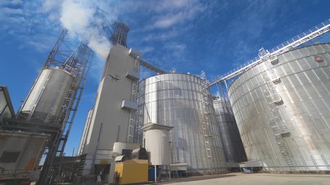 Agricultural Silos. Metal grain facility with silos. Storage and drying of grains, wheat, corn, soy, sunflower against the blue sky with white clouds