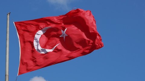 The red Turkish flag flies in the wind against a blue sky.