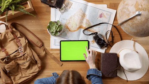 Top view of young woman with tablet with green screen and maps planning vacation trip holiday, desktop travel concept.