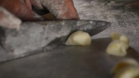 Gnocchi with potatoes. Old woman hand cutting rolls of potato dough for the preparation of homemade gnocchi. Traditional italian food from Rome, Sardinia, south of italy. 
