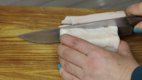 Woman cuts lard with a knife into slices on a wooden cutting board. Close-up copy space.