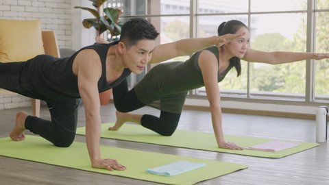 Happy Asian beautiful lifestyle family couple doing YOGA standing meditating on virabhadrasana 3 pose workout at home together on mat. Two people sport healthy concept