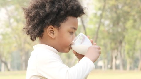 Little black skinned boy raise a glass of milk to drink for breakfast in the park.African american child concept,slow motion shot.